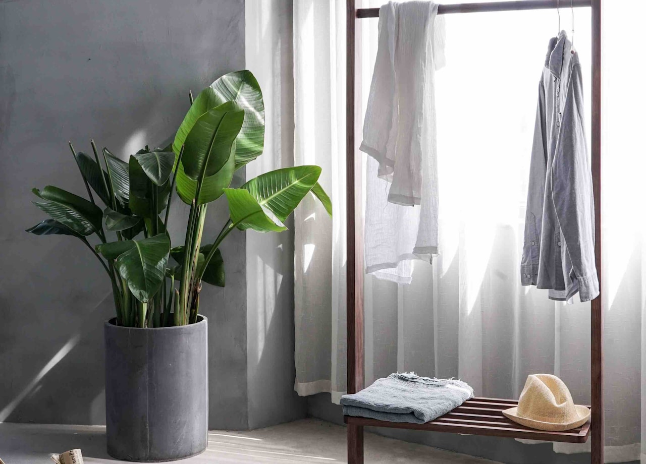 A grey dress shirt hanging on a wooden rack in front of a window